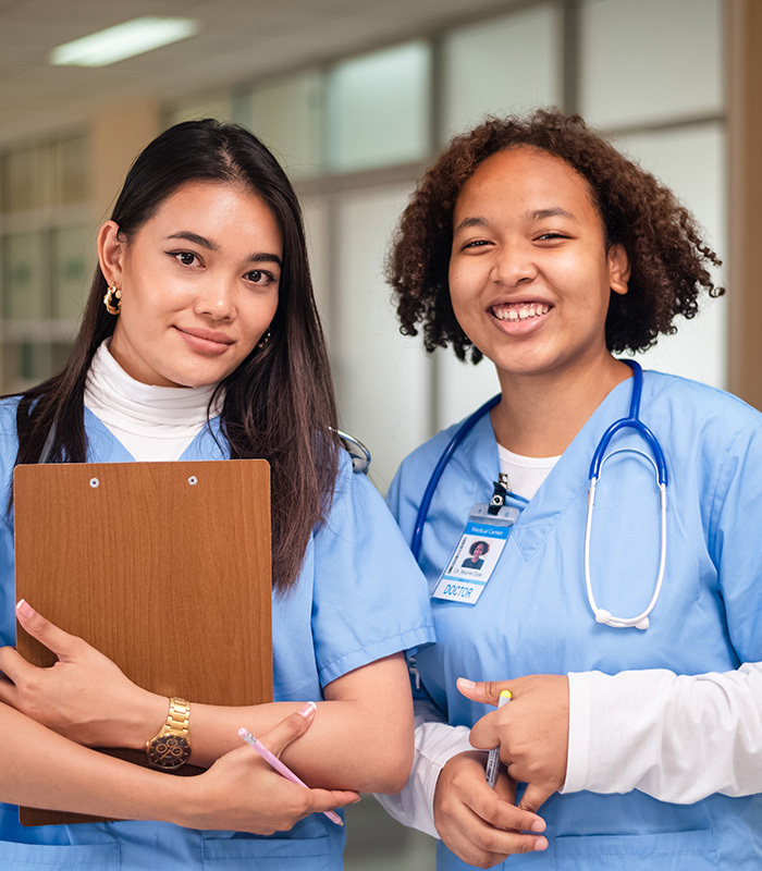 two smiling nurses holding pens and a clipboard